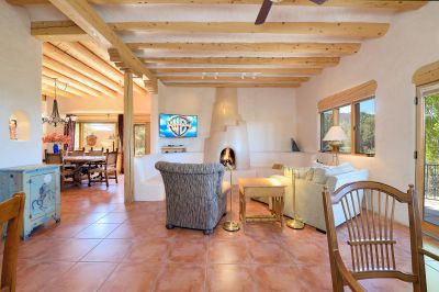 Comfortable, stylish family room has a central fireplace surrounded by built in custom bancos, and glorious views to the Jemez Mountain range,, and pink sunset skies under the portal.