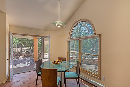 Breakfast Room Area with high canted ceiling, contemporary pendant light fixture, and French doors to the portal, terrace and fenced, wooded grounds