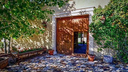 Cobblestone front entrance through custom wooden doors leading to the main house placita