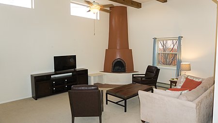 Living room with beams and ceiling fans with view of wood burning Kiva fireplace
