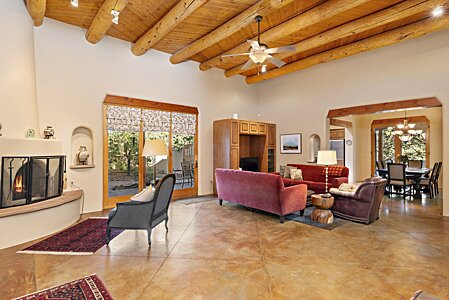 Large open Living room with vigas, Latillas, and Kiva fireplace with view over to formal Dining room.