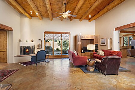Large open Living room with Vigas, Latillas, and Kiva fireplace and stained concrete flooring.